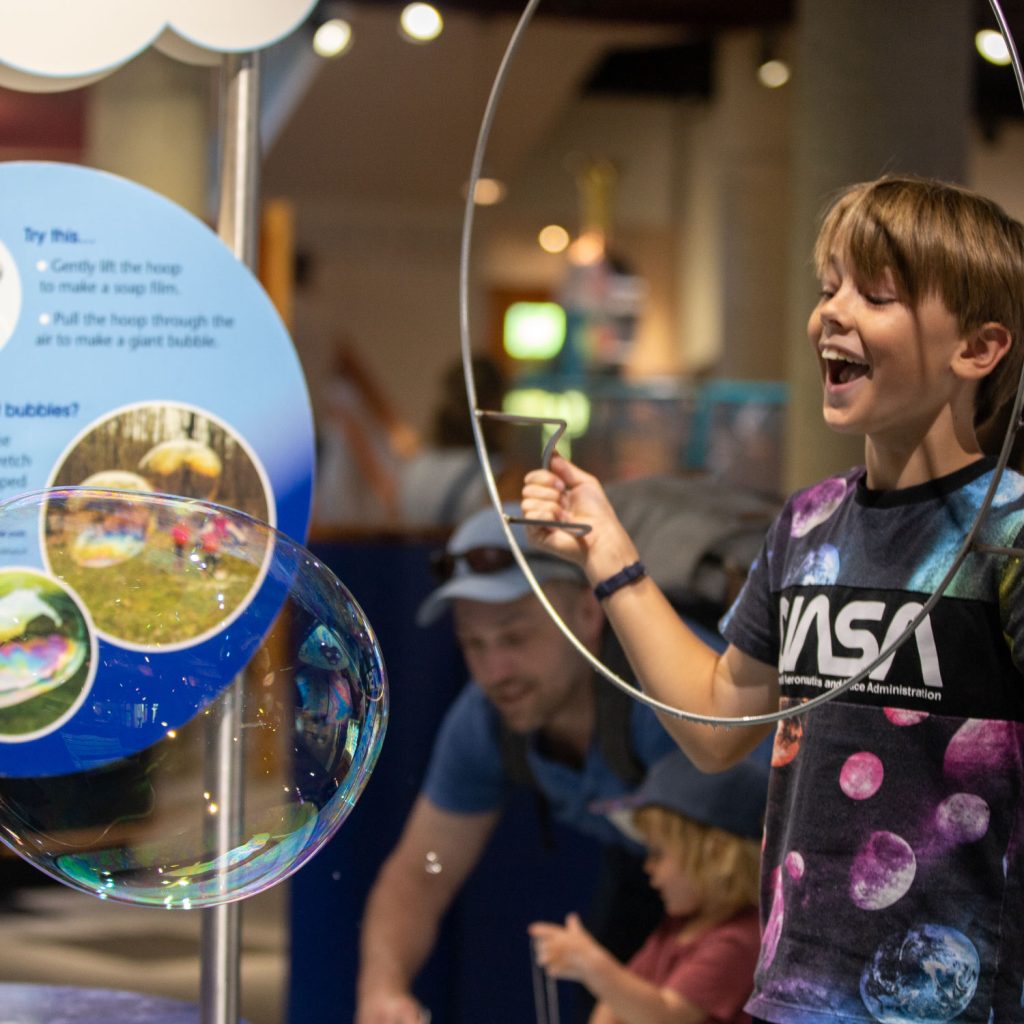 Square image of a young visitor enjoying a large soap bubble
