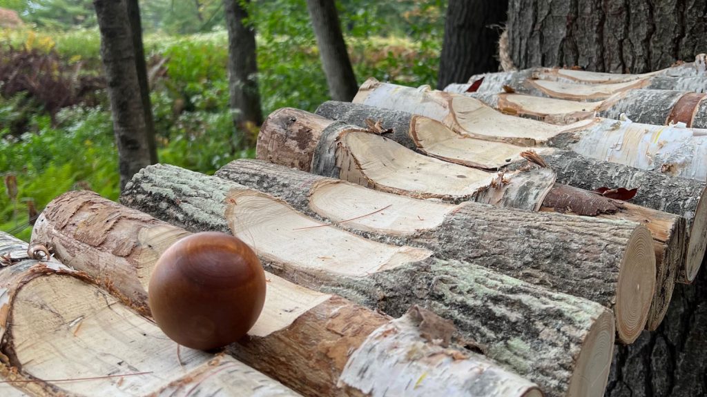 A wooden ball rolls down a panel of inclined logs, carved to create a ball chute
