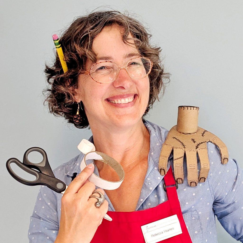 An educator poses with a cardboard model of Thing while holding scissors and tape